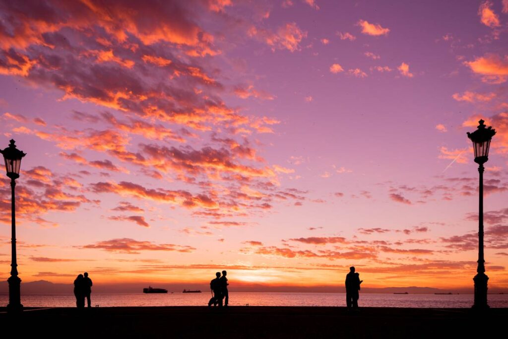 Silhouettes of people enjoying a walk by the seaside of the town during sunset